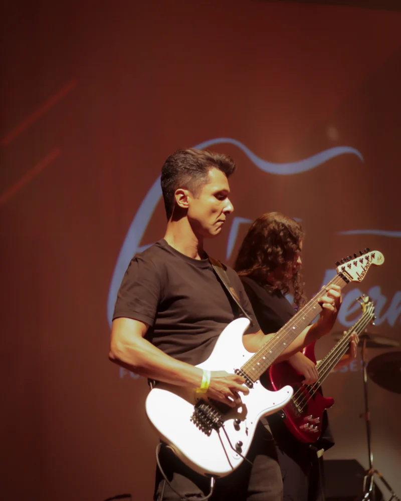 Aluno adulto do Espaço Fermata tocando guitarra no palco